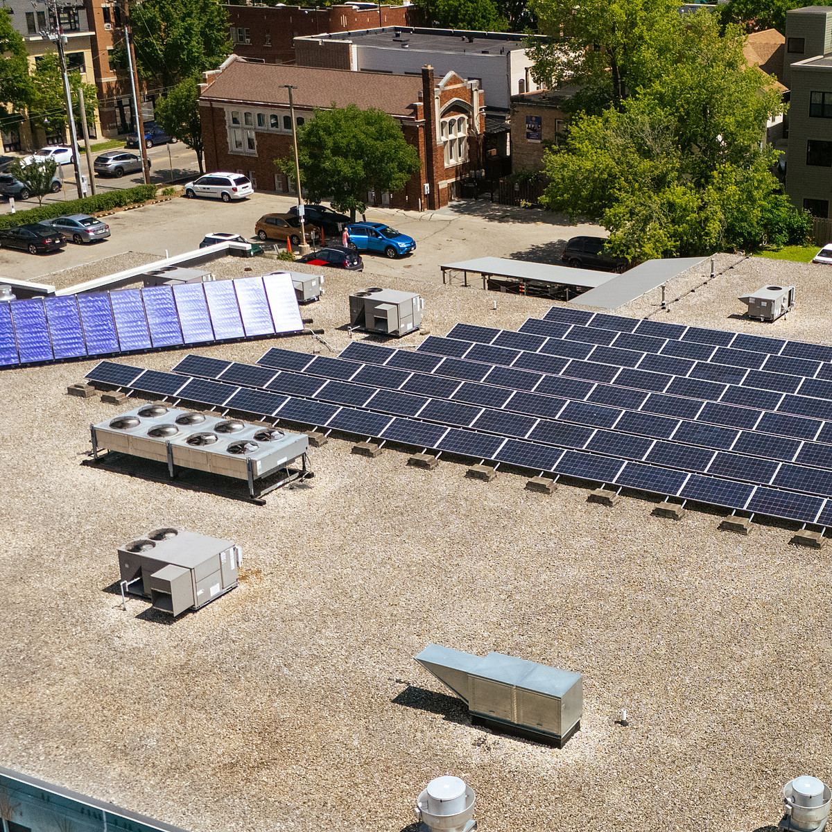 Ballasted solar array on a commercial flat roof, with rooftop units and a downtown street behind it