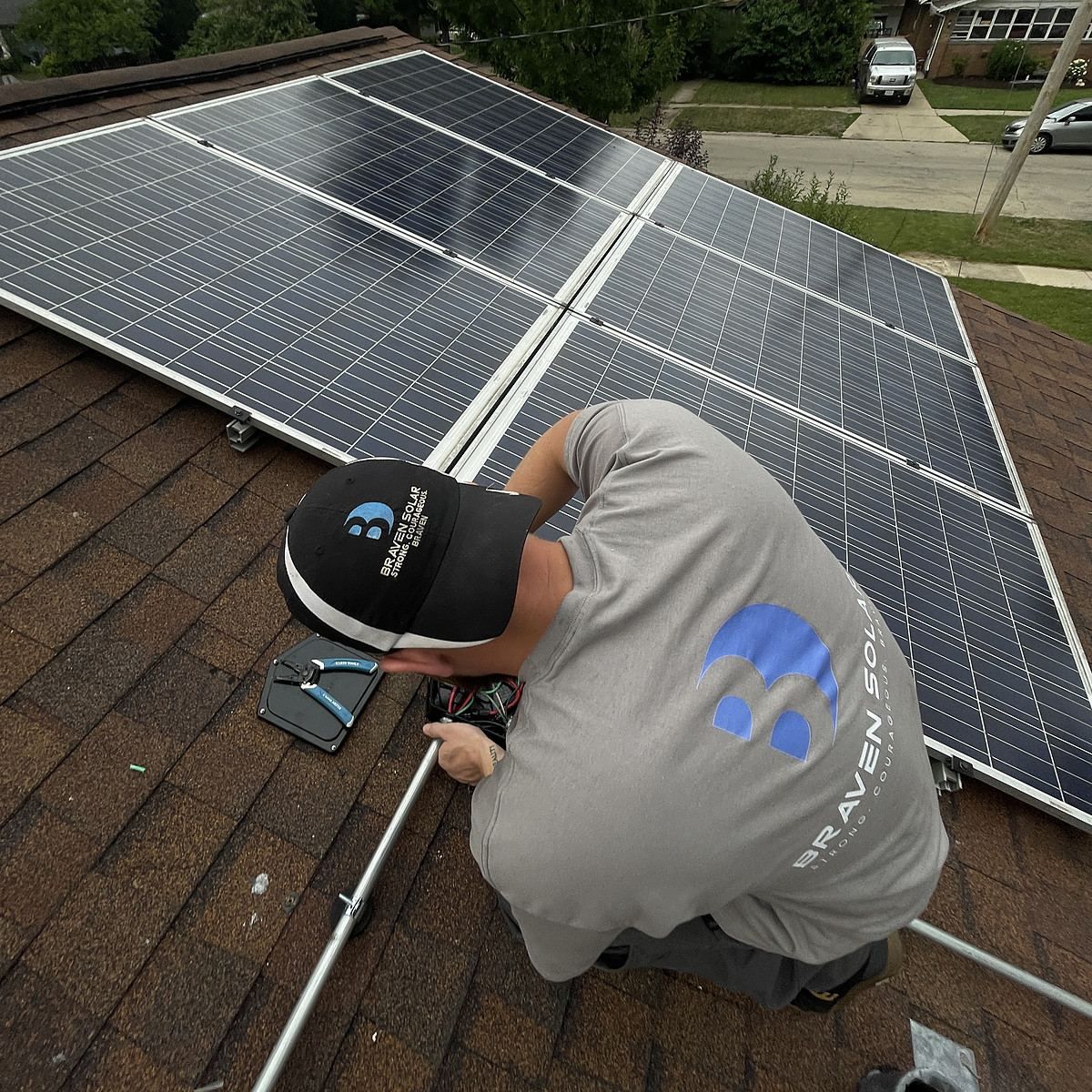 Installer kneeling on a roof beside a solar array with the street behind