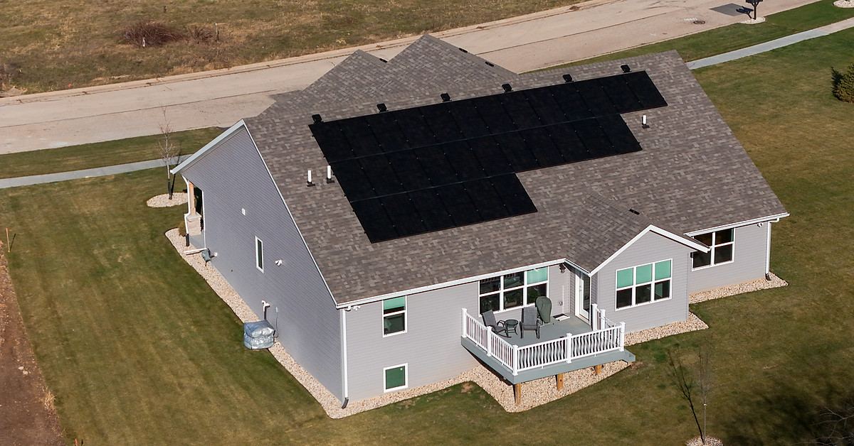 Aerial view of a ranch home with a rooftop solar array and an open lawn